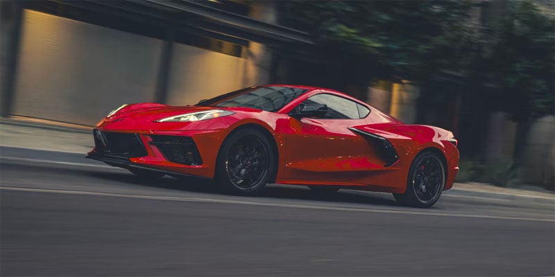 A sleek, red Corvette C8 with black wheels drives at an angle on a city street.